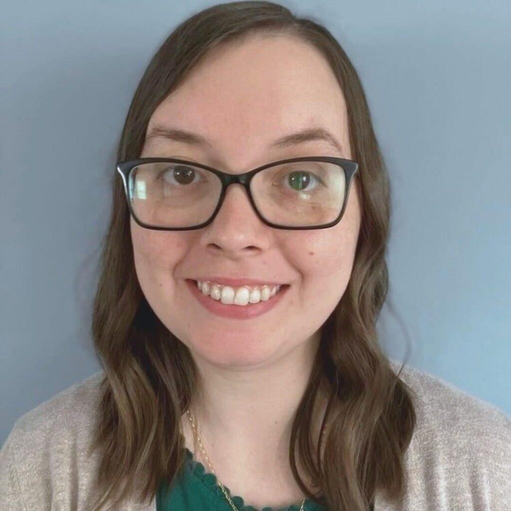 Kristin Gunner, Virtual Assistant for small business owners, smiling with glasses, long brown hair, wearing a teal top and beige cardigan, against a plain light blue background. Appears friendly and approachable.