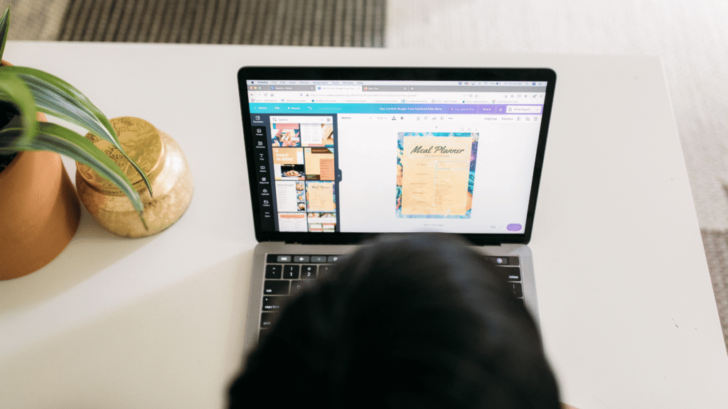 A virtual assistant focused on a laptop, designing a graphic with various tools and resources on the screen.