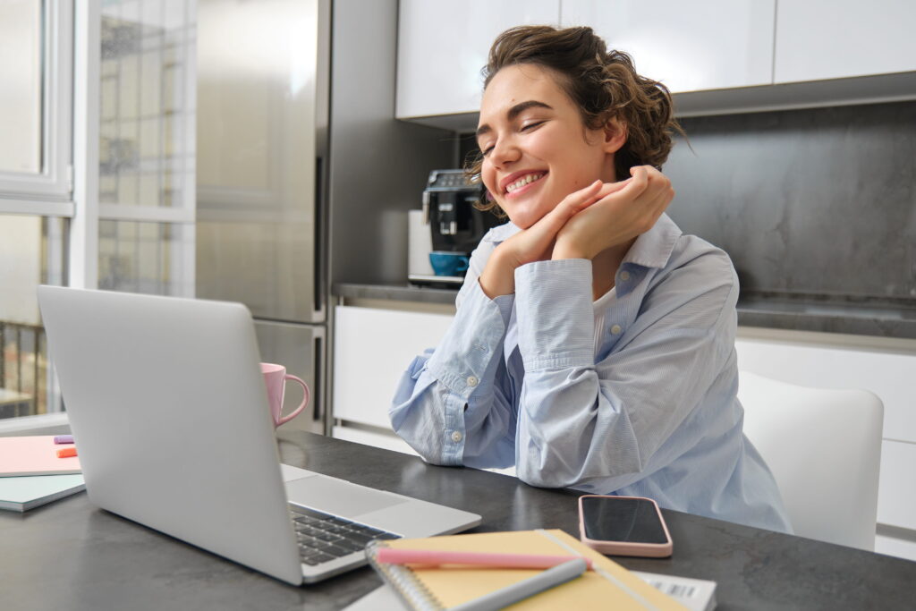 A woman seated at a desk, focused on her laptop while working in a well-lit office environment.